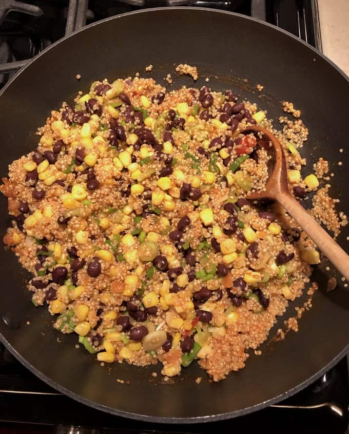 Cooking quinoa, black beans, corn, green onions with salsa in skillet.