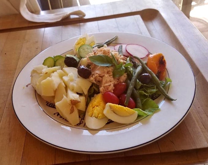 Tuna nicoise salad with potato, hard boiled eggs, green beans and tuna on white plate.
