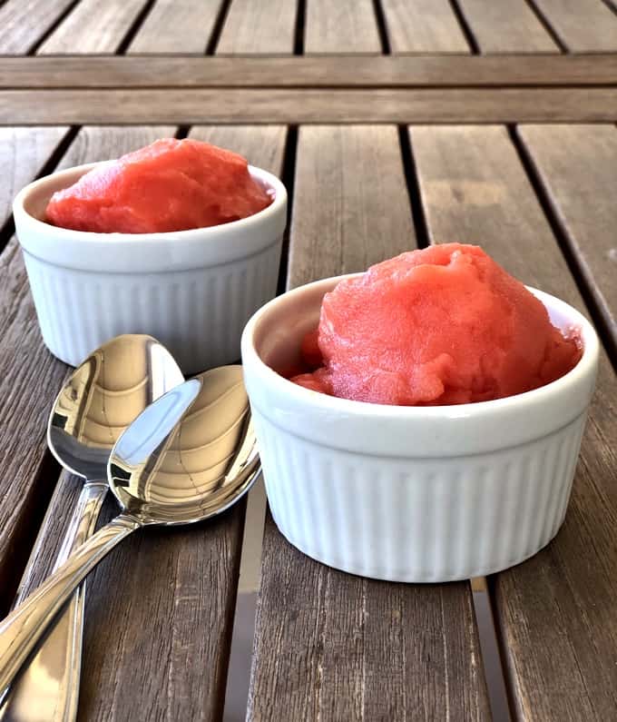 Watermelon lime sorbet in two white ramekins with spoons on wooden table.