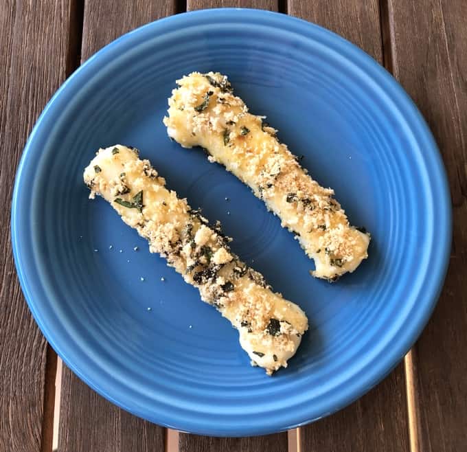 Two baked mozzarella cheese sticks on blue plate on wooden table.