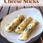 Three baked mozzarella cheese sticks on pottery plate on wood table.