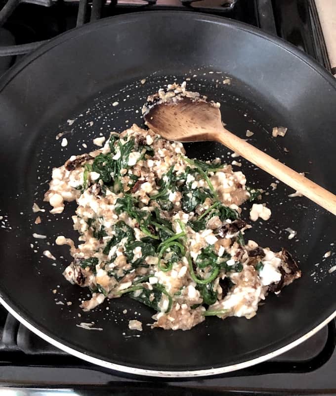 Mixing cottage cheese with cooked mushroom mixture in skillet with wooden spoon.