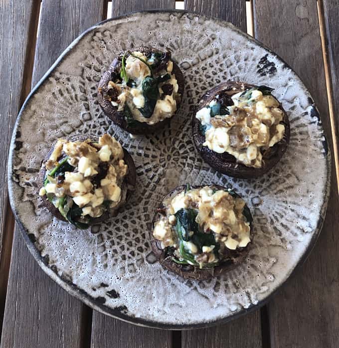Vegetarian stuffed mushrooms on decorative pottery on wooden table from overhead.