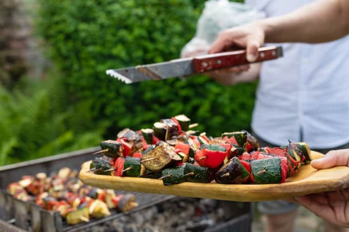 Removing ratatouille vegetable skewers from grill to platter with tongs.