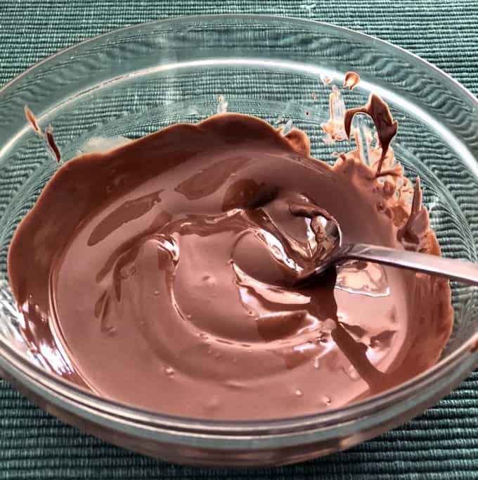 Melted chocolate in small glass bowl with spoon on green placemat.