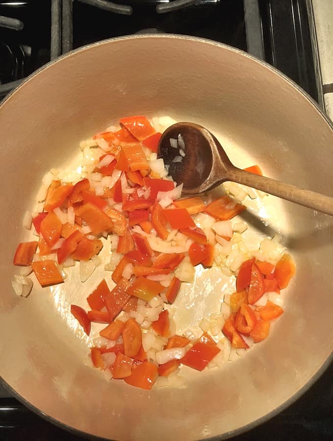 Cooking chopped onion and red bell pepper in skillet with wooden spoon.
