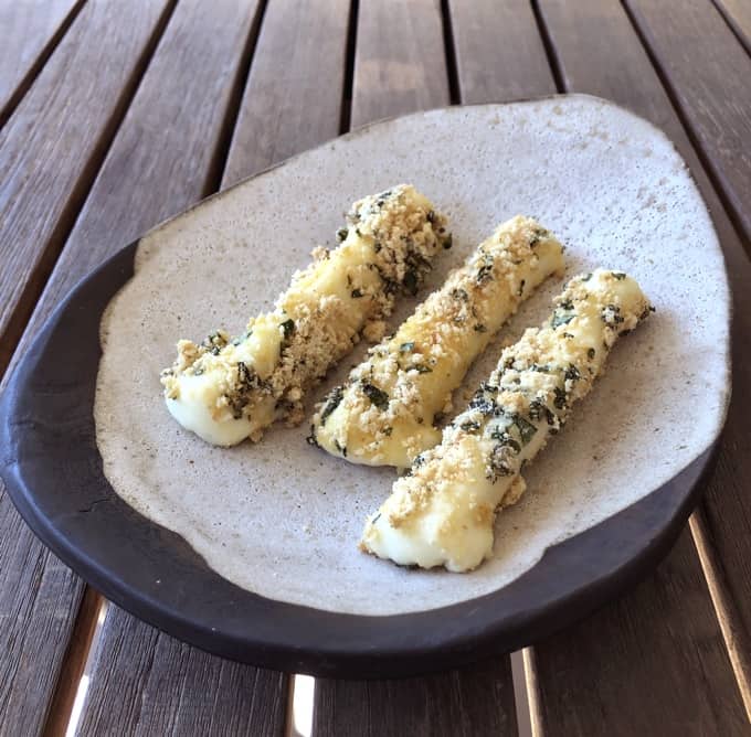 Baked mozzarella cheese sticks on potter plate on wooden table.