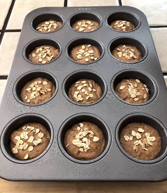 12-cup muffin pan with vegan banana oat muffin batter topped with sprinkle of oats.