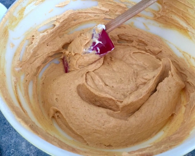 Folding cool whip whipped topping into pumpkin mousse with red spatula.