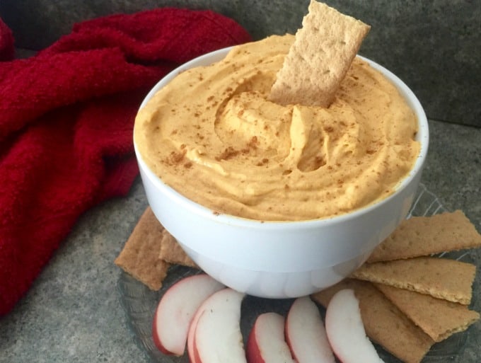 Skinny Pumpkin Mousse Fluff sprinkled with ground cinnamon in white bowl with apple slices and graham crackers for dipping.
