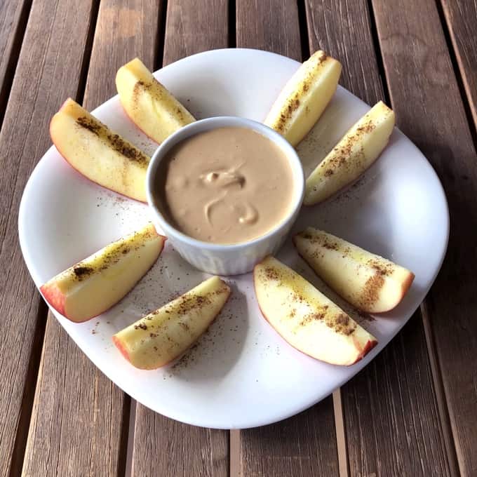 Apple Cinnamon "Fries" with creamy peanut butter dip on white plate on wood table.