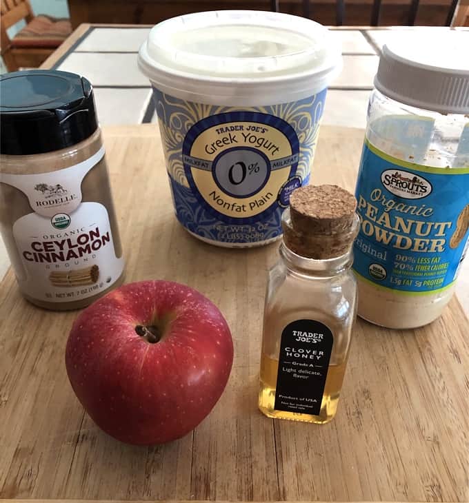 Cinnamon, plain Greek yogurt, peanut powder, honey and a fresh apple on bamboo cutting board for making apple fries with peanut butter dip.
