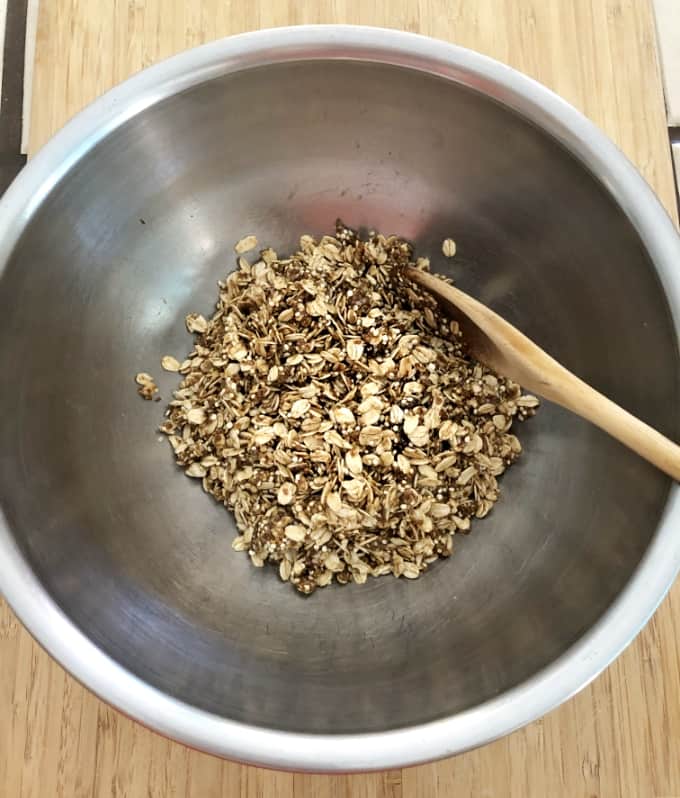 Stirring quinoa oat granola ingredients in mixing bowl with wooden spoon.