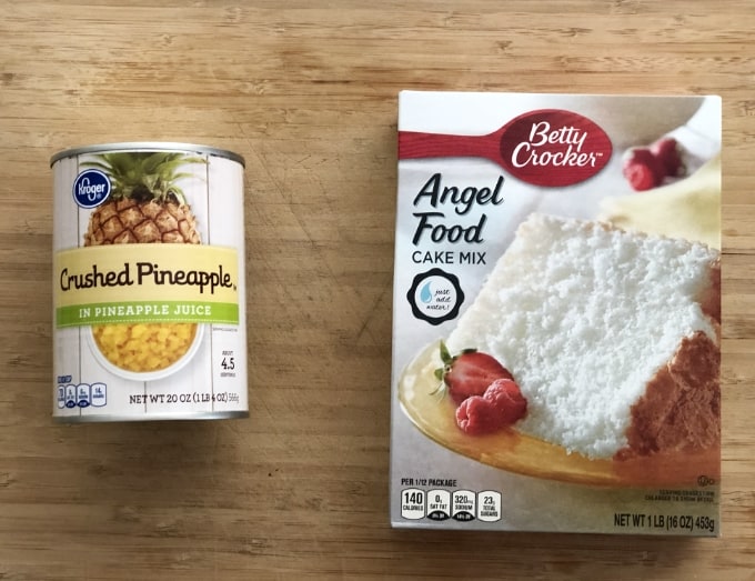 Can of crushed pineapple and box of angel food cake mix on bamboo cutting board.