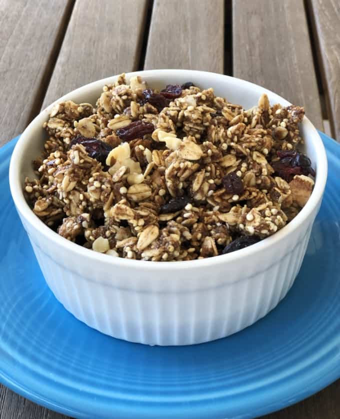 Quinoa oat granola with dried cranberries, raisins and walnuts in white bowl on blue plate.