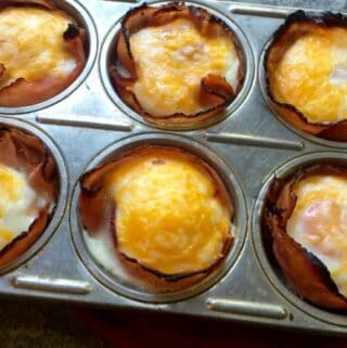 muffin tin with whole eggs baked in sliced deli ham lined cups topped with cheese and baked
