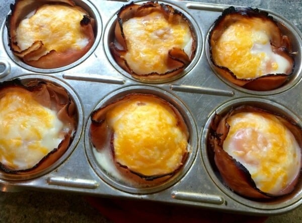 muffin tin with whole eggs baked in sliced deli ham lined cups topped with cheese and baked