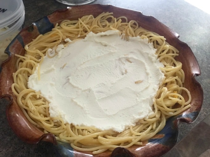 Ricotta cheese spread over spaghetti in ceramic pie plate.