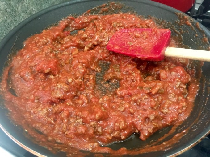 Stirring meat sauce in skillet with spatula.