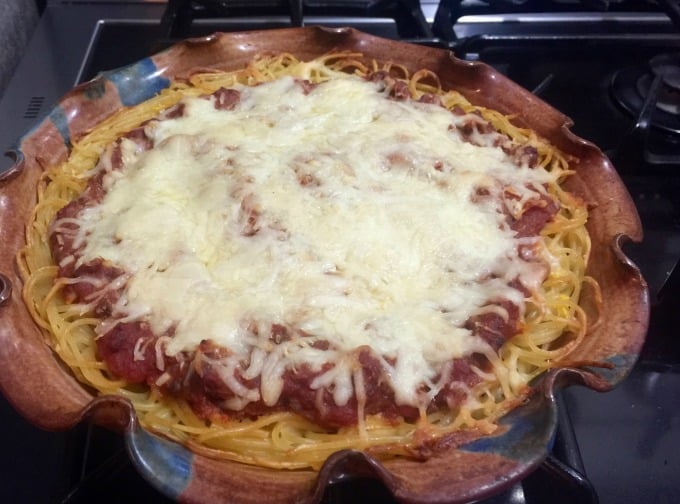 Baked pizza pasta pie with spaghetti, meat sauce and mozzarella cheese in ceramic baking dish.