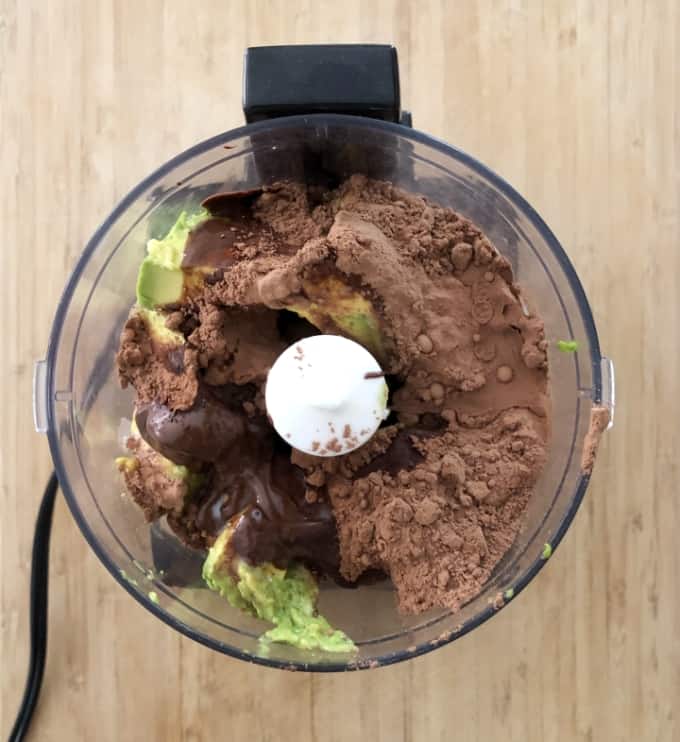 Cocoa powder, melted chocolate, avocado, maple syrup, cinnamon and salt in food processor for making dark chocolate avocado mousse.