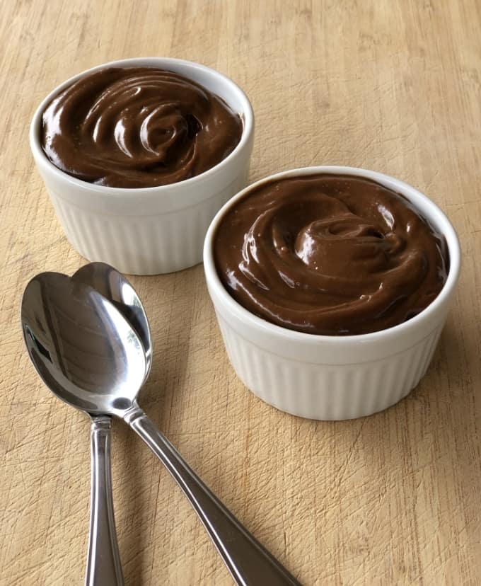 Chilled dark chocolate avocado mousse in white ramekins with two spoons.