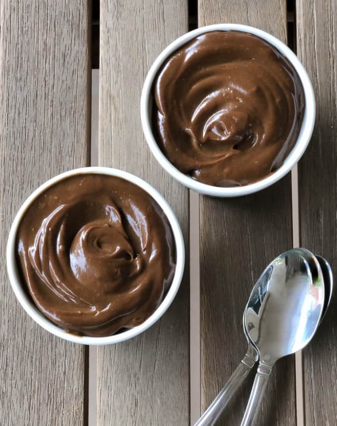 Dark chocolate avocado mousse in ramekins with two spoons on wooden table.