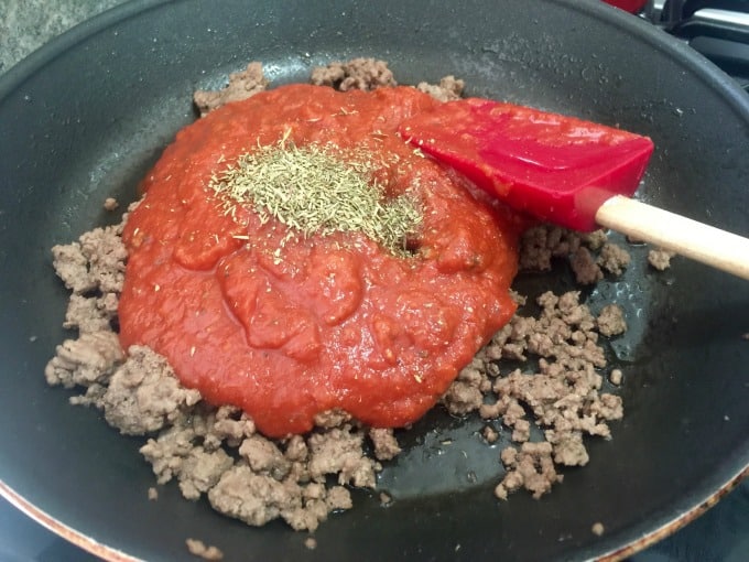 Cooking ground beef in a skillet with tomato sauce and and oregano.