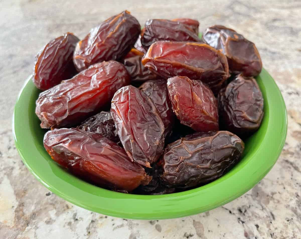 Whole Medjool Dates in a green bowl on granite.