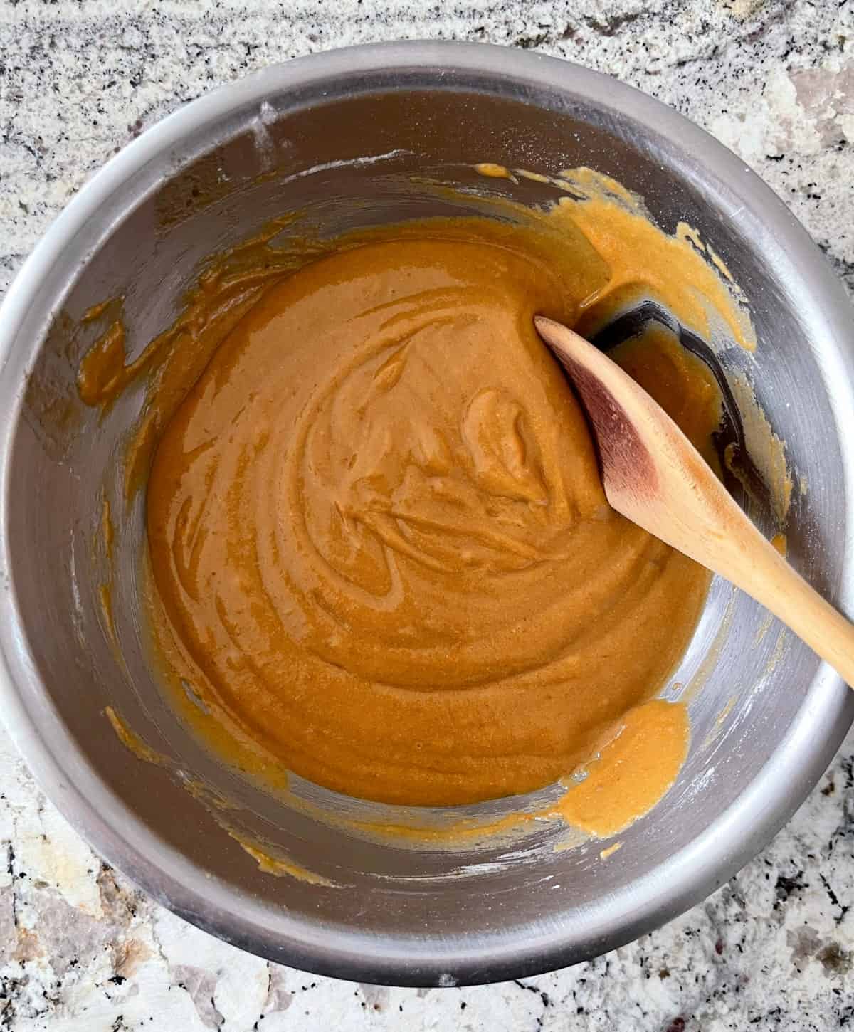 Mixing cookie bar batter in a mixing bowl with a wooden spoon.