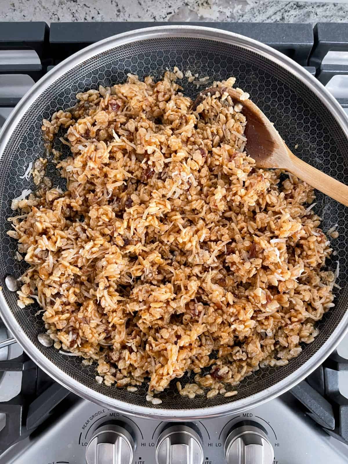 Combining Rice Krispies date balls mixture in a skillet with wooden spoon.