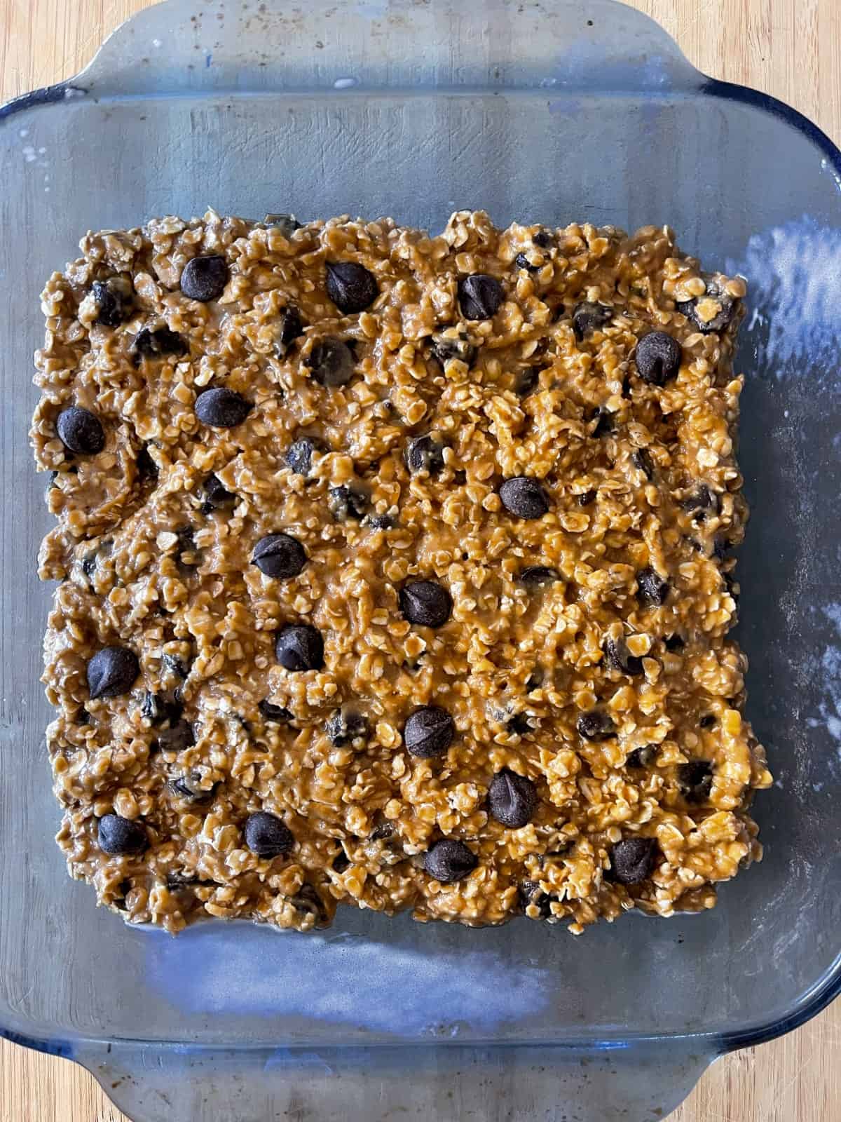 Unbaked oatmeal chocolate chip cookie bars in blue glass baking dish.