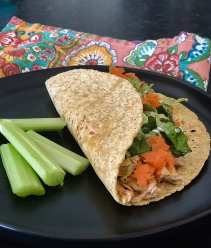 Buffalo chicken blue cheese tortilla wrap with celery sticks on black plate.