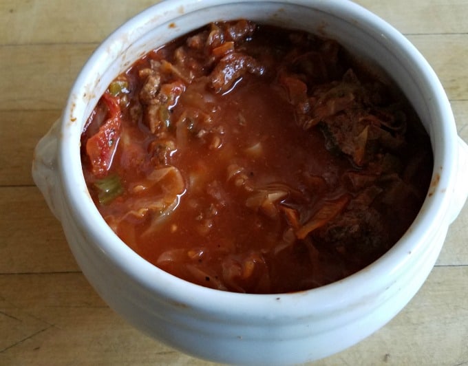 Cabbage roll soup in white bowl on wooden counter.