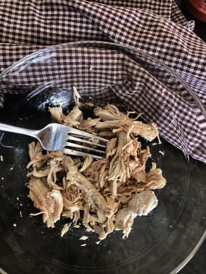 Shredded chicken mixed with hot wing sauce in small glass bowl.