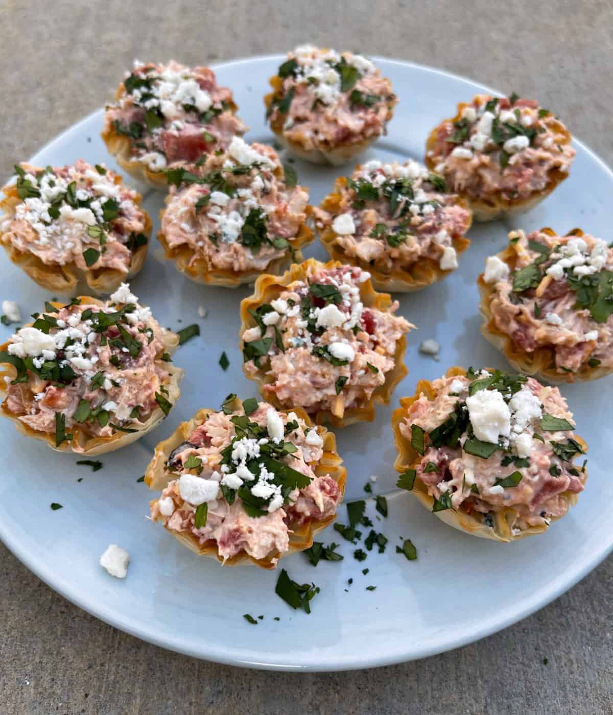Mini Buffalo Chicken Bites garnished with blue cheese crumbles and chopped cilantro on a round blue plate.