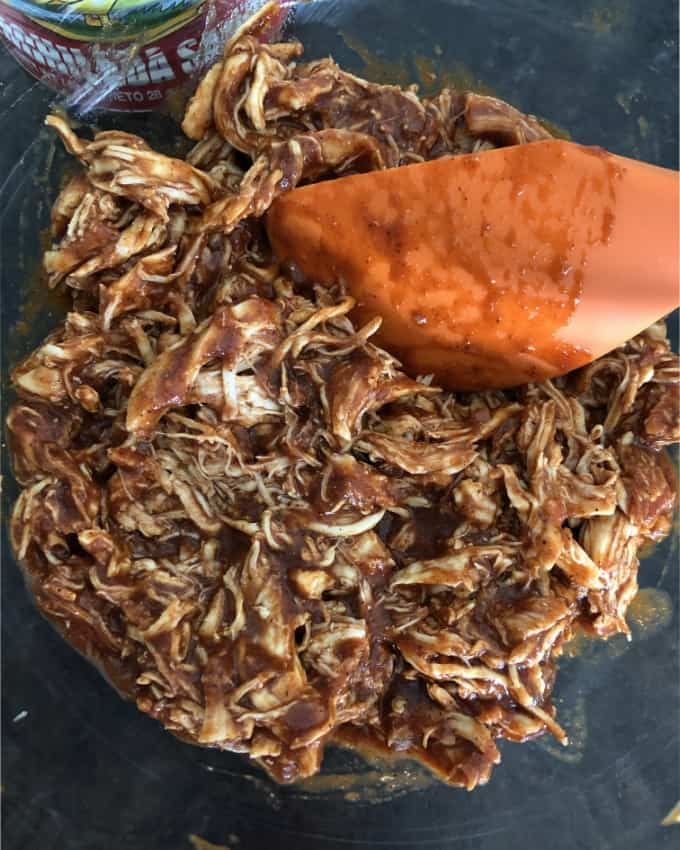 Mixing shredded chicken with red enchilada sauce.