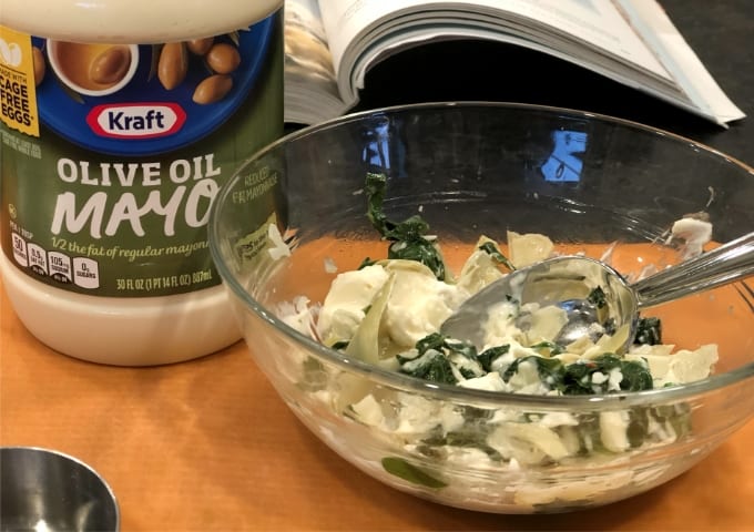 Mixing spinach artichoke dip in small glass bowl with olive oil mayo.