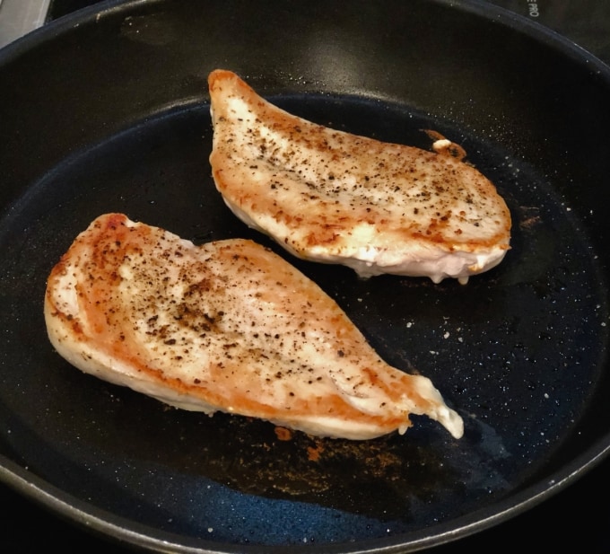 Cooking two thin chicken breasts in skillet on stovetop.