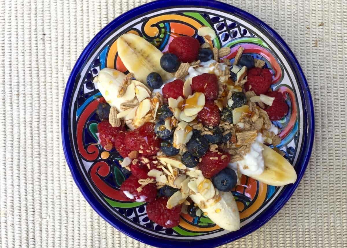 colorful ceramic plate with cottage cheese, sliced bananas, raspberries and blueberries from above