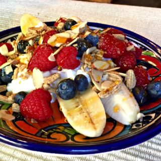 sliced bananas and berries with a dollop of cottage cheese and sprinkling of granola on colorful pottery plate