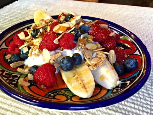 sliced bananas and berries with a dollop of cottage cheese and sprinkling of granola on colorful pottery plate
