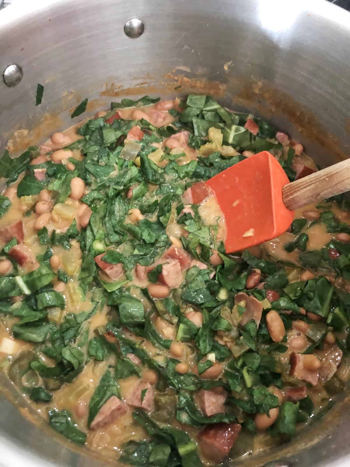 Stirring chopped spinach into stock pot of bean soup with spatula.