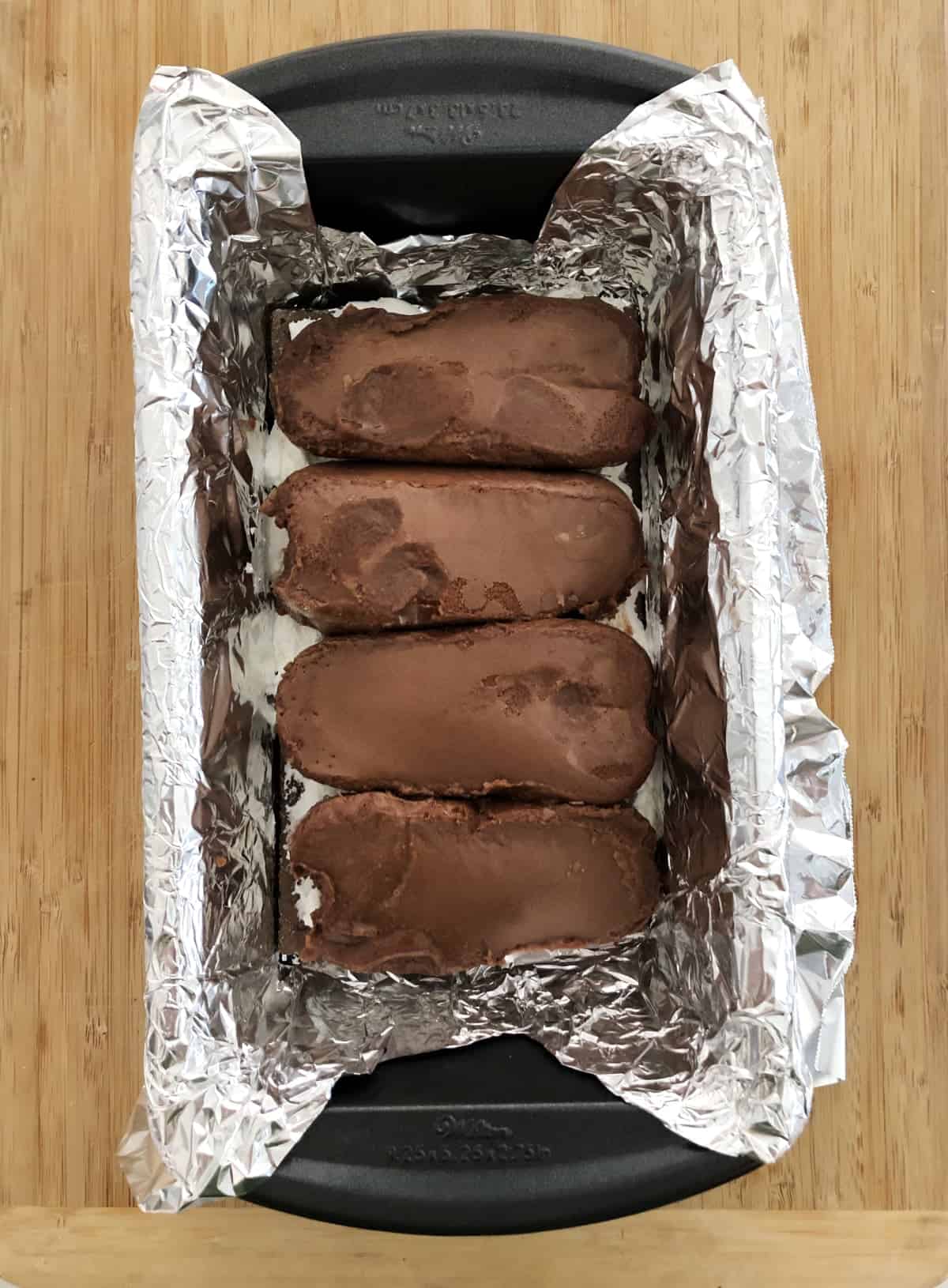 Four chocolate fudge ice cream bars side-by-side in foil lined loaf pan.