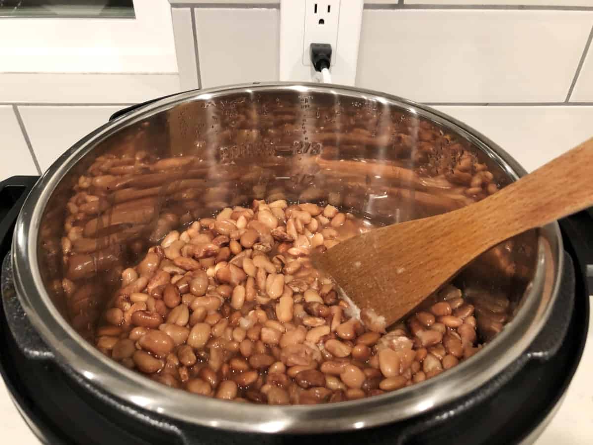 Stirring cooked pinto beans in Instant Pot with wooden spoon
