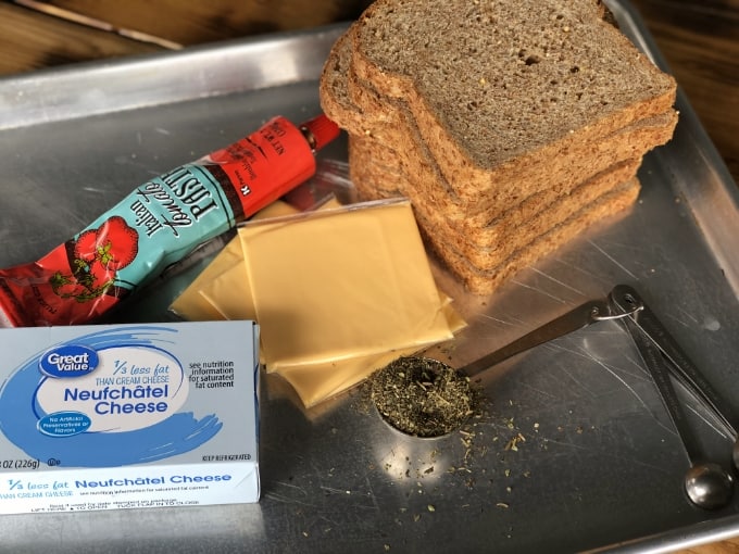 Ezekiel bread, cream cheese, tomato paste and cheese slices on kitchen counter.