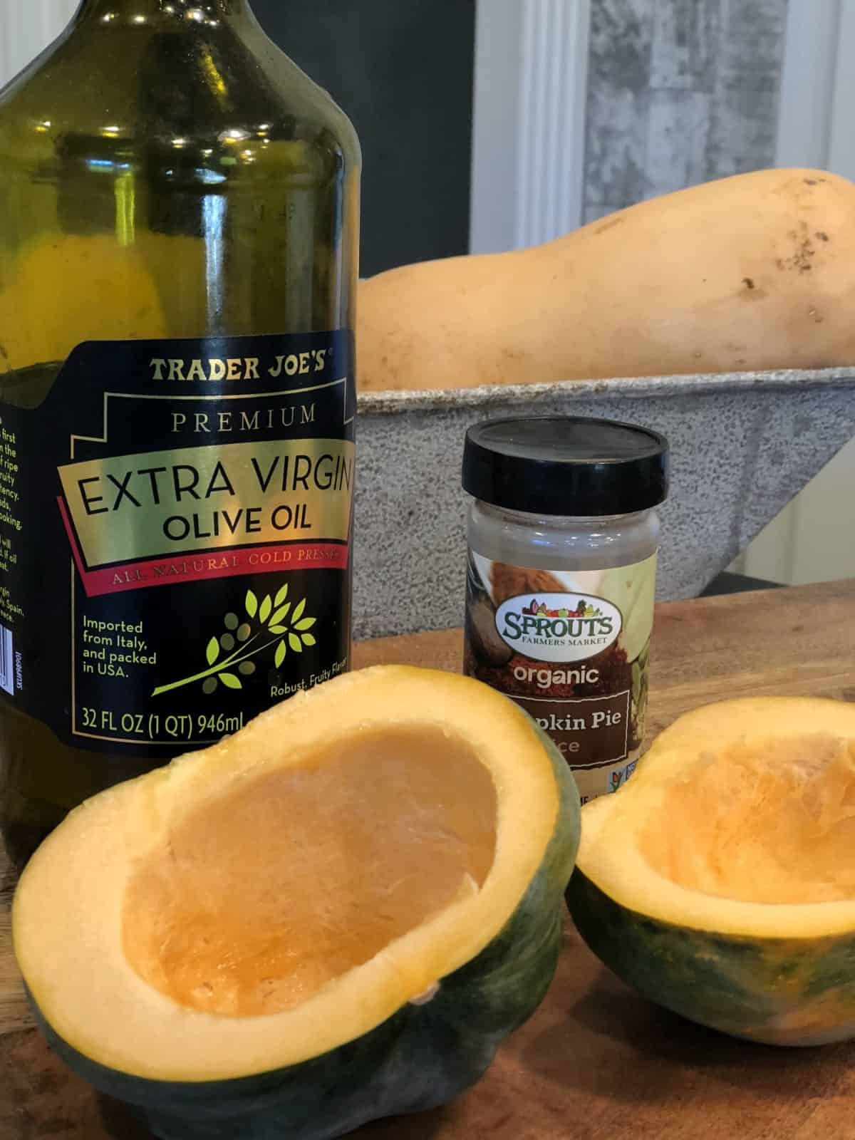 Halved acorn squash with bottle of olive oil and pumpkin pie spice.
