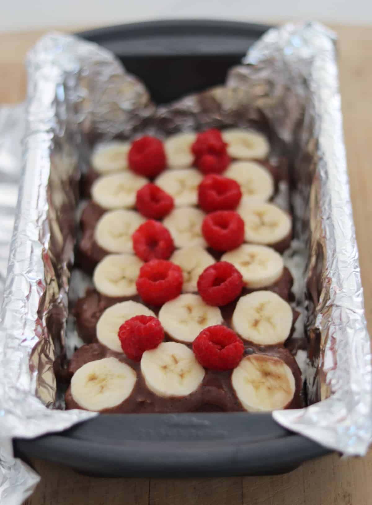 Chocolate fudge ice cream bars with sliced bananas and fresh raspberries in foil-lined loaf pan.