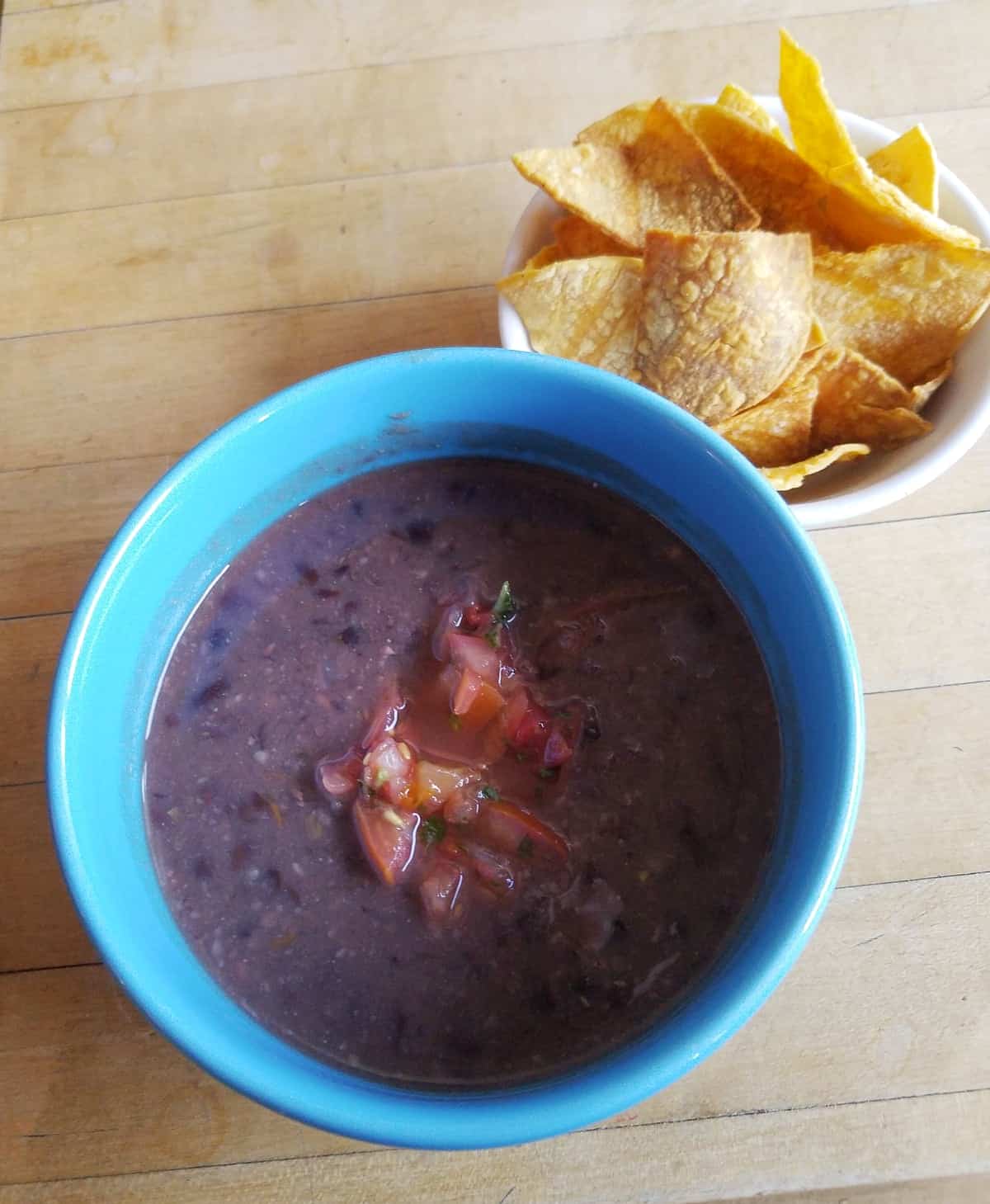 Instantpot black bean soup topped with pico de gallo in blue bowl next to tortilla chips.