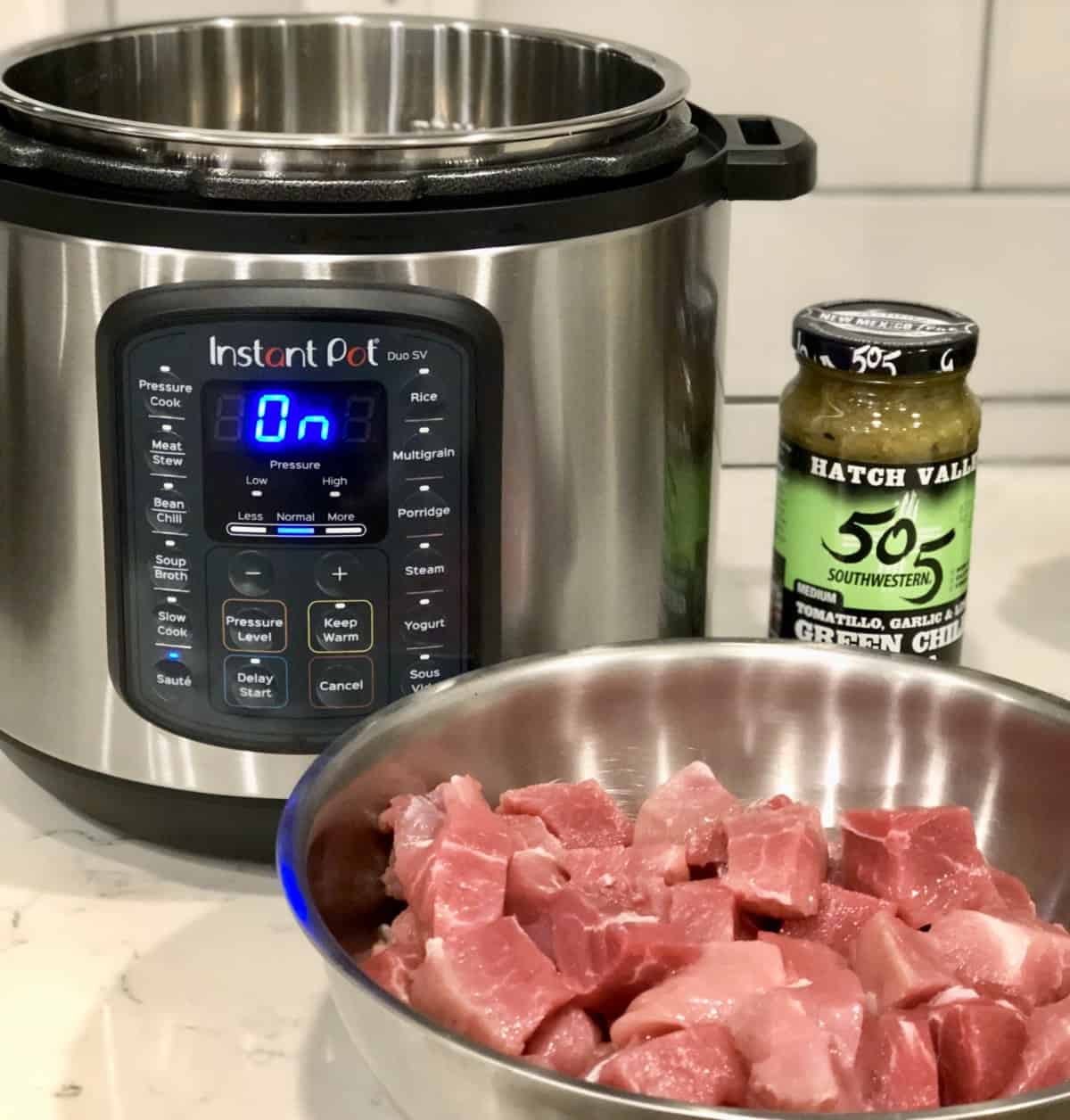 Instant Pot with jar of salsa verde and cubed pork in stainless steel bowl